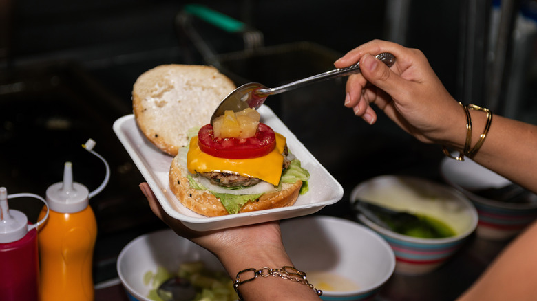 A chef topping a cheeseburger with pineapple.