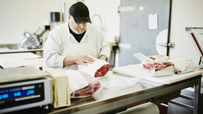 A butcher prepping raw beef next to a scale