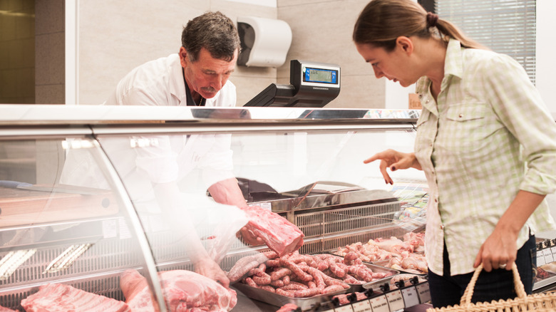 A woman shopping and talking to a butcher in front of a raw meat display