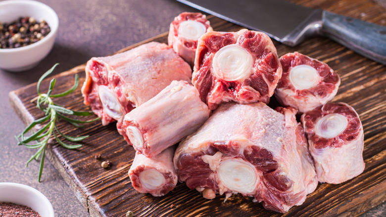 Pieces of raw oxtails on a wooden board next to a knife and seasonings