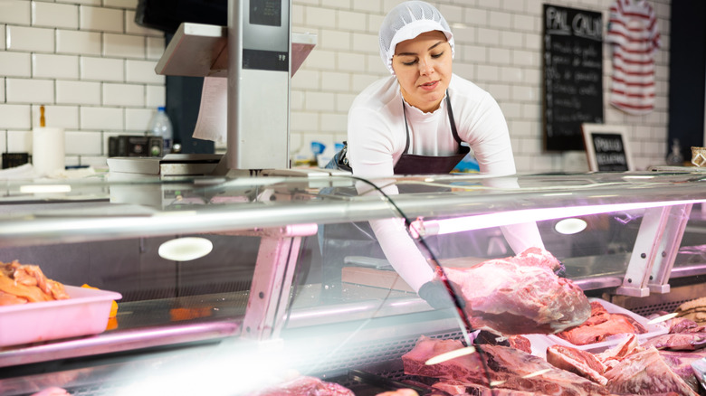 A female butcher lifting a heavy primal piece of raw meat from a case