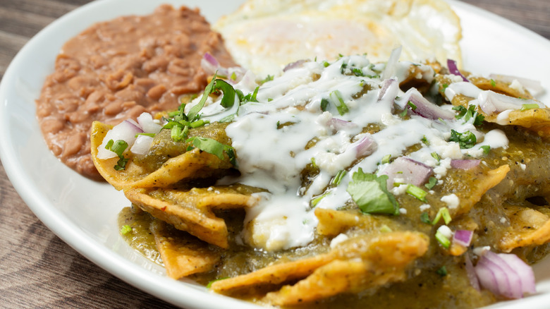 Close-up photo of chilaquiles in green sauce with beans and an egg