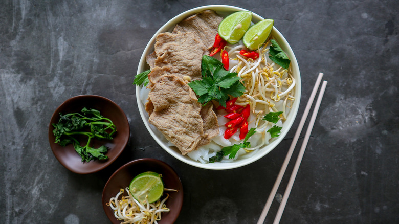 Plate of pho with chopsticks and dishes of garnishes