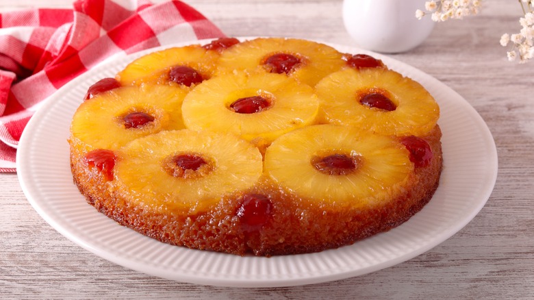 uncut pineapple upside down cake sitting on a white plate on a table