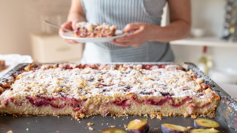 berry sheet cake sitting on table with woman holding plate with cake behind the table