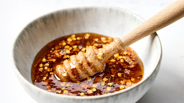 Hot honey with chili flakes in a bowl that also has a wooden honey dipper utensil resting on the side