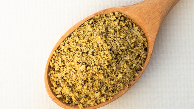 Lemon pepper in a wooden spoon on a white background