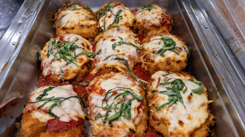 Nine pieces of chicken Parmesan with herbs and red sauce in a broiler pan