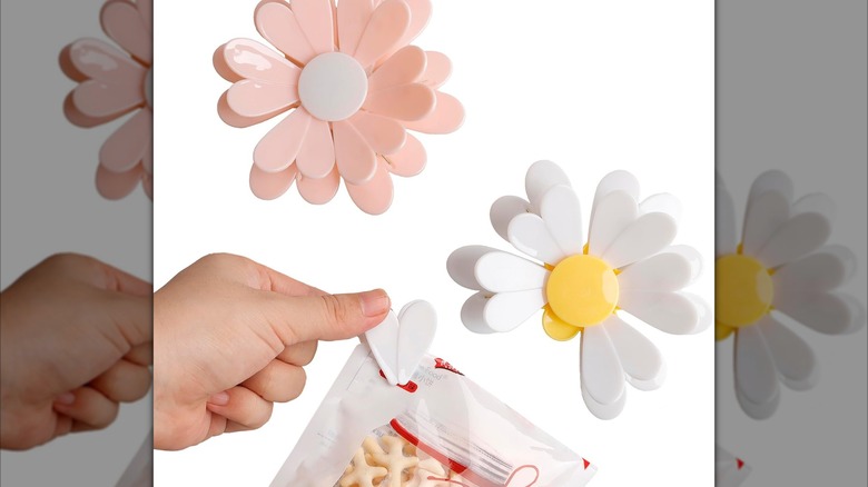 Pink and white daisy-shaped bag clips, one clip is being used on a white bag of food