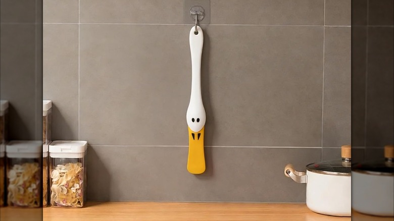 Long white and yellow spatula shaped like a duck bill hanging on the wall in a modern kitchen