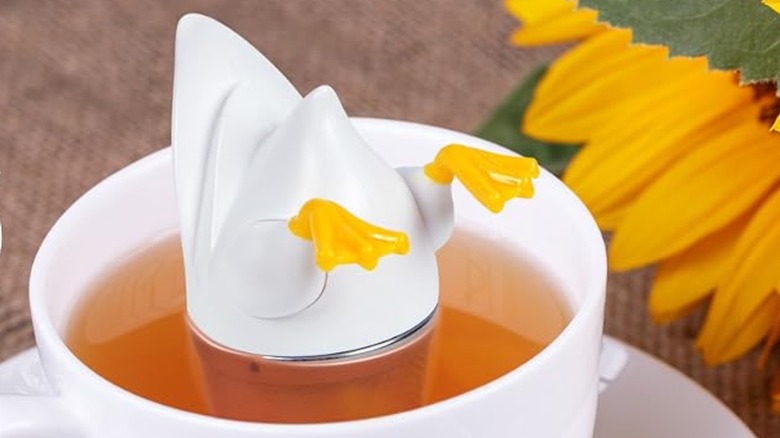 Tea infuser shaped like a head-down duck in a cup of tea next to a sunflower