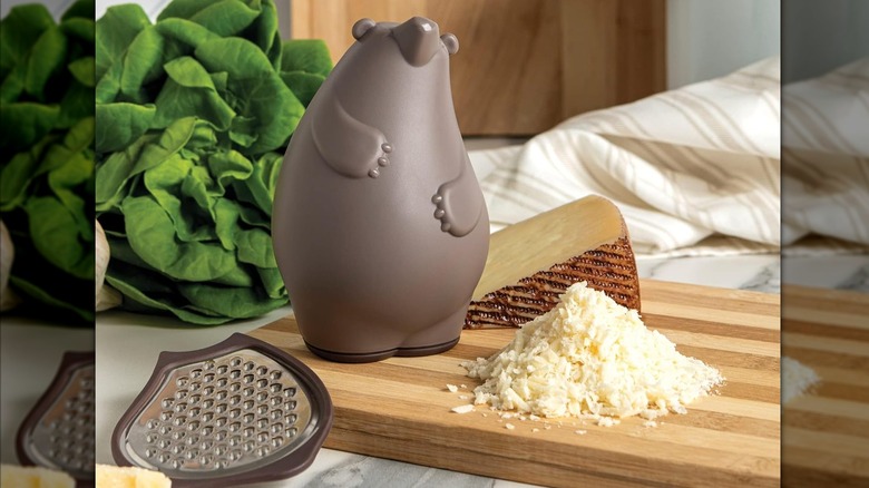 Bear-shaped cheese grater on a wooden cutting board next to a cheese wedge and pile of grated cheese