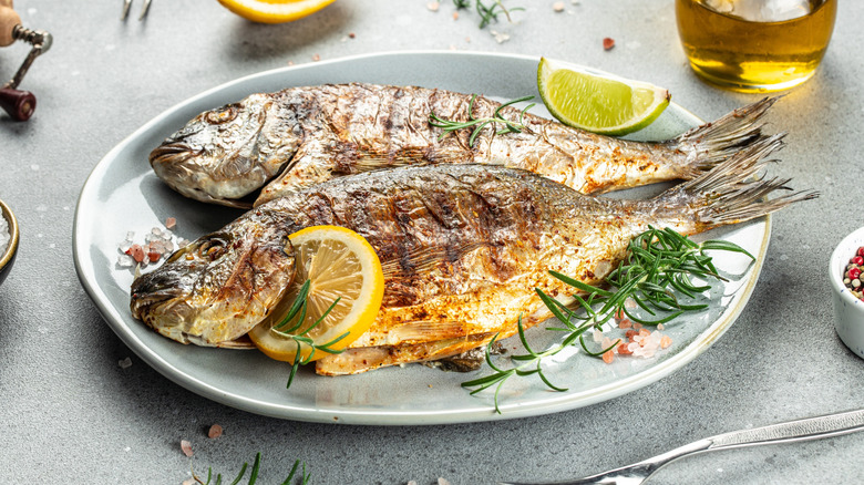Two whole grilled fish on a plate with lemon