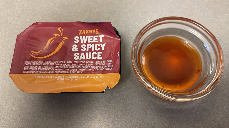 A packet of Sweet & Spicy Sauce sits on a gray counter next to a dish of orange, slightly translucent sauce.