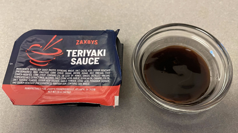 A packet of Teriyaki Sauce sits on a gray counter next to a dish of dark brown sauce.