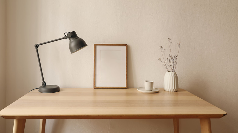 A minimalist Scandivanian home decor of a desk, painting, and vase arranged beside a mug