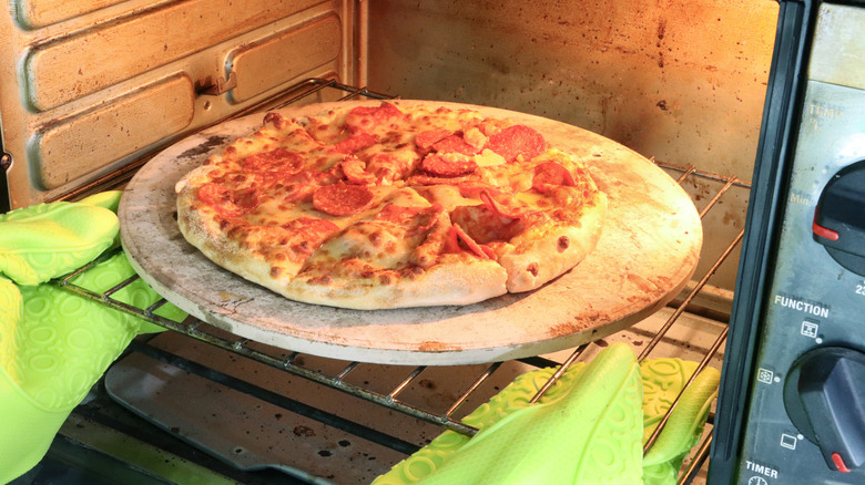Person putting a pepperoni pizza into the oven on a baking stone