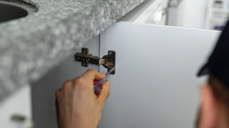 A repairman installing hinges with a screwdriver