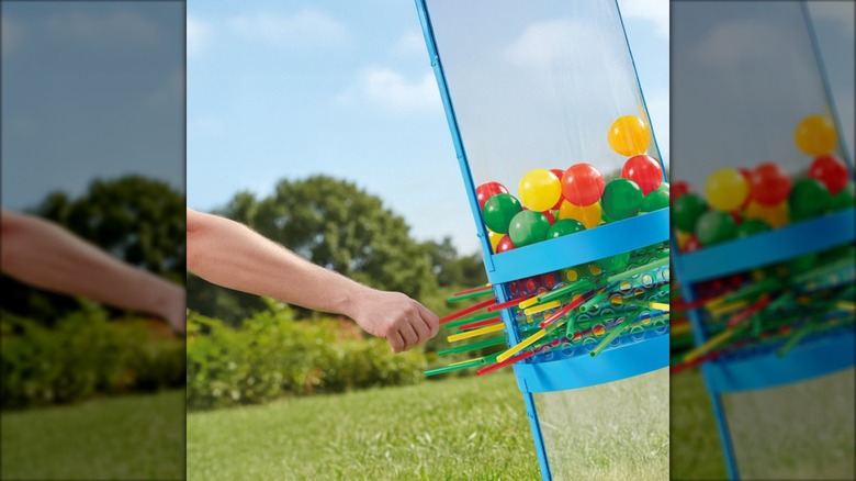 Side view of a person's hand pulling a colorful stick out of a giant lawn kerplunk game.