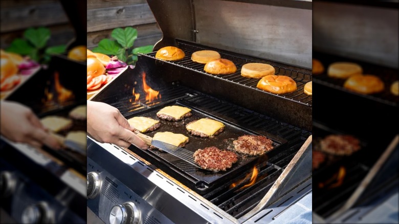 A person grilling burgers on top of the Lodge Cast Iron Reversible griddle top from Costco.