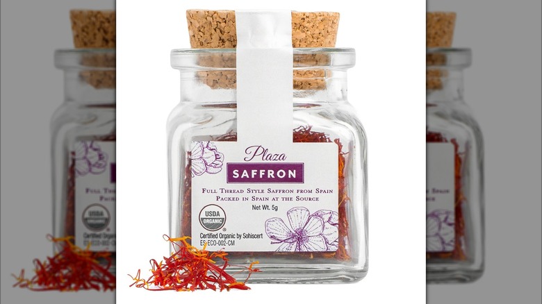 A jar of full thread saffron from Spain with pieces of saffron in front of it.