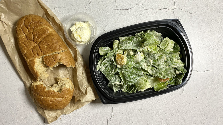 Longhorn Steakhouse's Caesar Salad in a takeout container next to a loaf of half-eaten bread with butter in a container