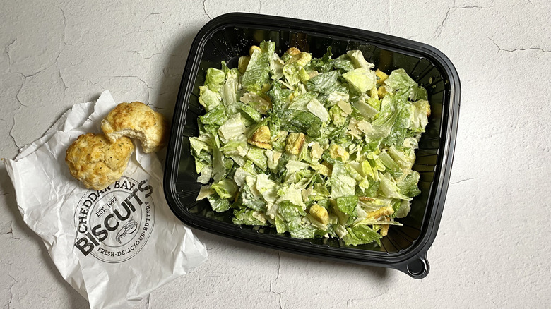 Red Lobster's Caesar Salad in a takeout container next to biscuits on a bag