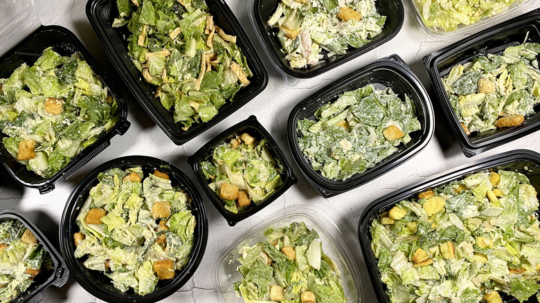 Assorted restaurant takeout Caesar salads in their containers on a white surface