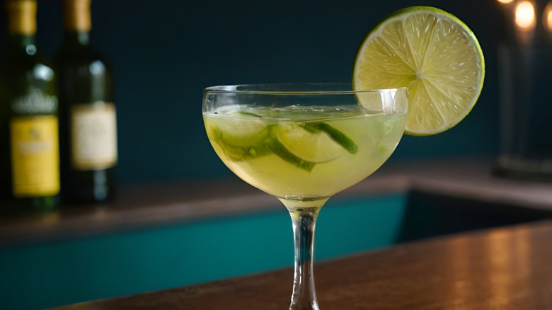 A coup with a green cocktail garnished with a lime wheel