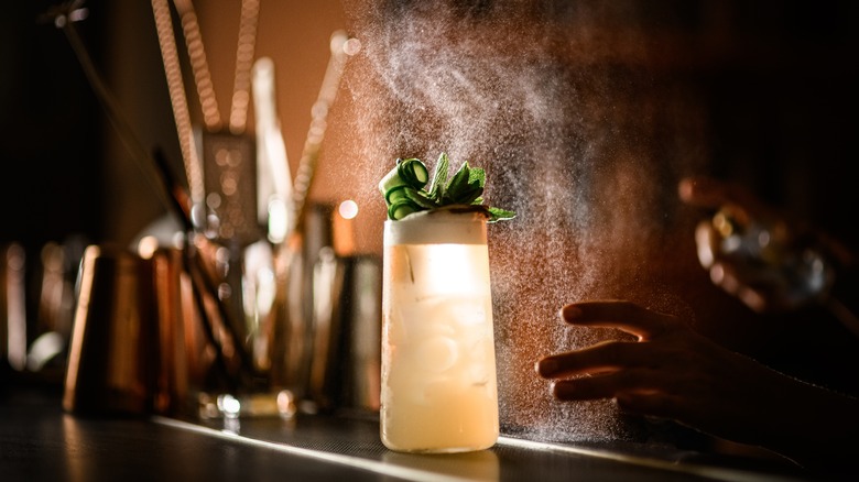 Fizzing pink highball with green garnishes on a bar