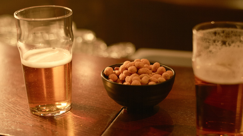 A bowl of bar nuts between two beers on a bar counter