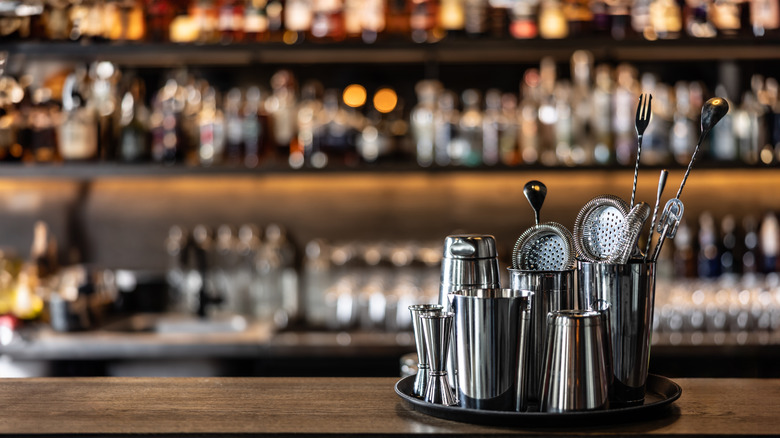 Mixology instruments sits on top of a bar with blurred bottles in the back