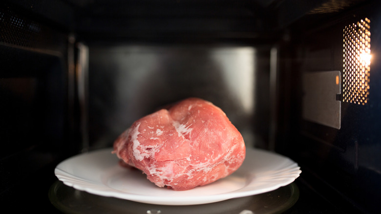 A piece of raw meat on a plate inside a microwave