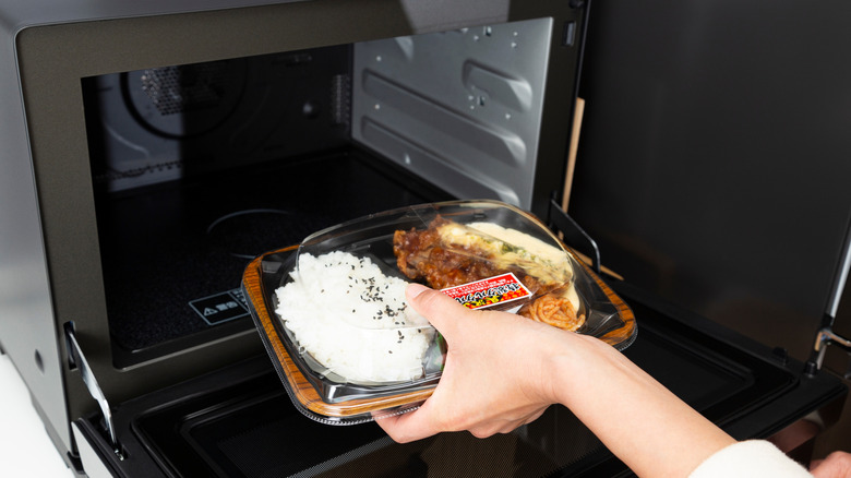 Hand placing a plastic container of food in the microwave