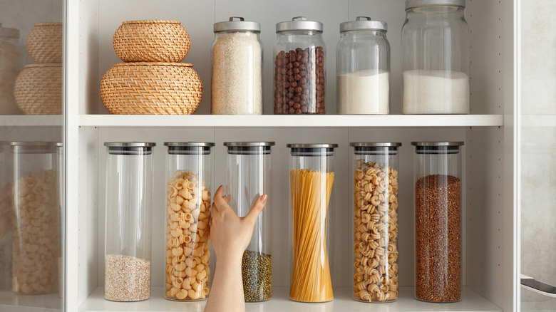Hand grabbing glass jar full of dry legumes from pantry