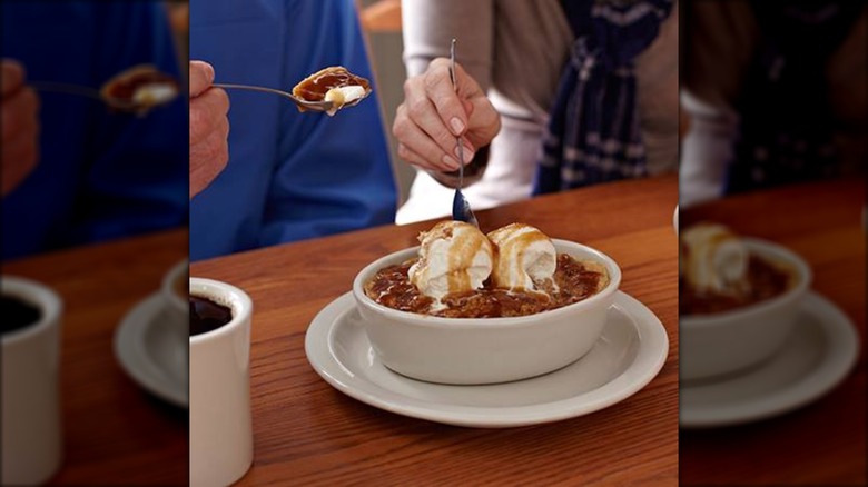 Two people are sharing Cracker Barrel's Baked Apple Dumplin topped with ice cream and caramel