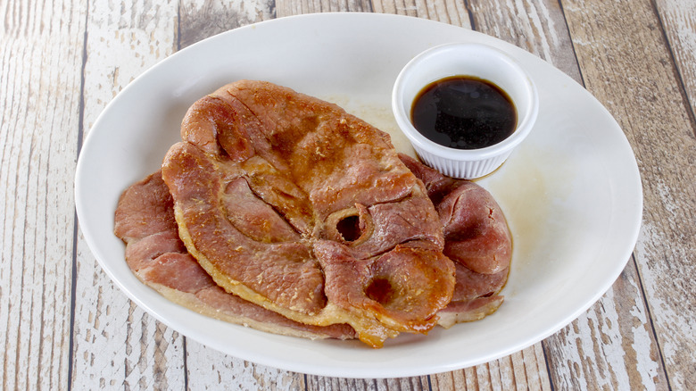 A plate of country ham served with a cup of red-eye gravy on the side