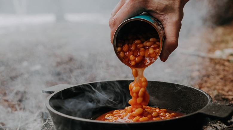 A person pouring a can of beans into a skillet