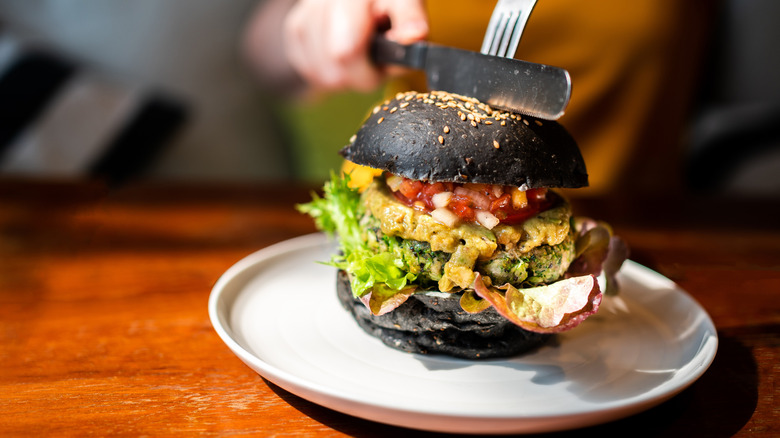 Knife cutting into a veggie burger with guacamole and mango salsa