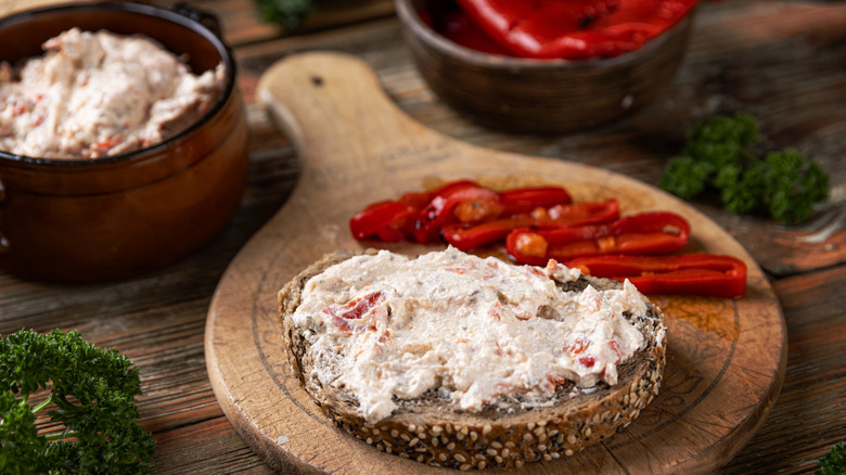 Slice of bread with cream cheese and roasted red peppers on the side