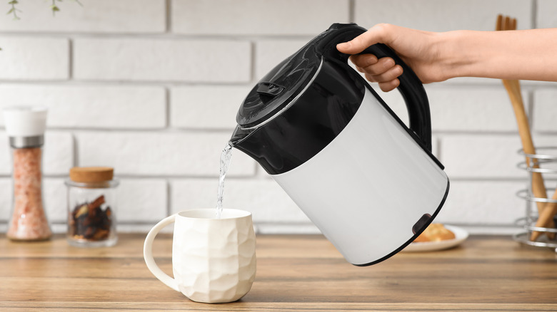 Person pouring an electric kettle into a mug