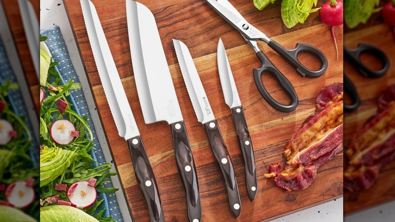 Set of knives on a wood board surrounded by salad and bacon