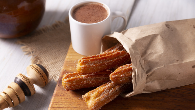 A bag of churros next to a cup of hot chocolate