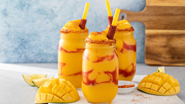 Three mangonadas on a counter with sliced mangos