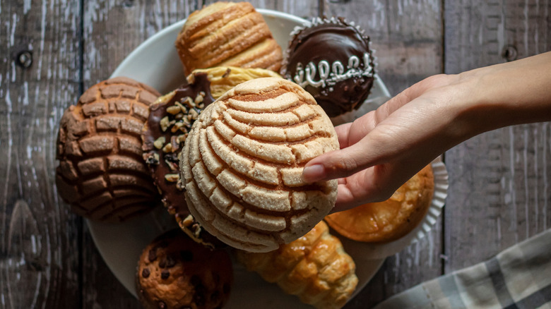 A person taking a concha from a plate of pan dulces