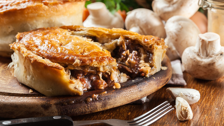 A meat pie with a slice cut out on a cutting board