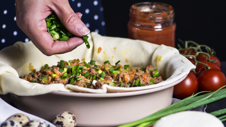 A person adding green onions to a meat pie