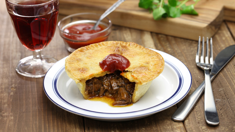 An Aussie meat pie cut open with a spoonful of ketchup on top