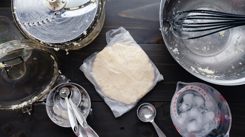 Pie dough wrapped in plastic next to baking tools