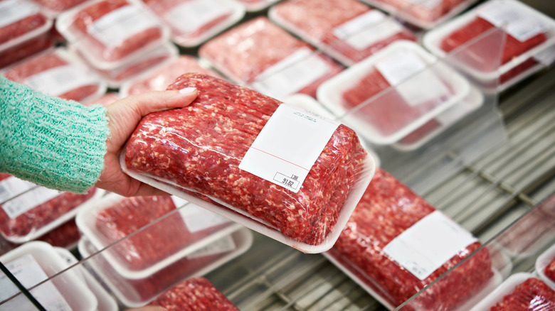 A person holding a package of ground beef at a grocery store